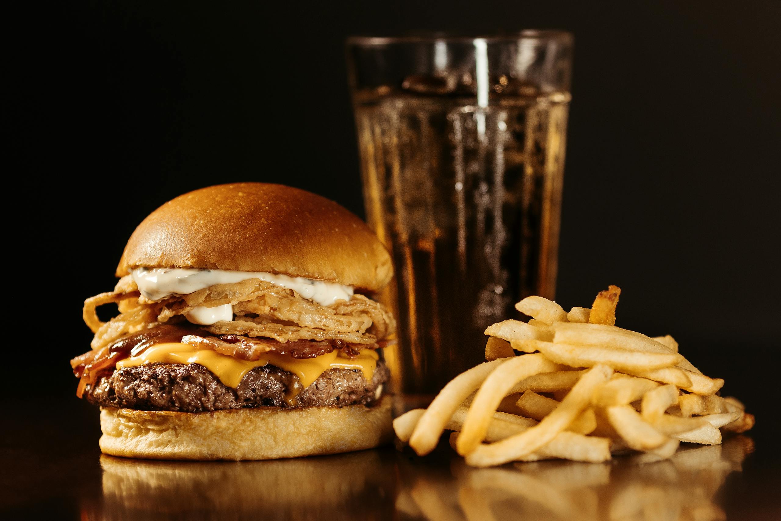Close-up of a juicy cheeseburger with fries and a soda, perfect for fast food enthusiasts.