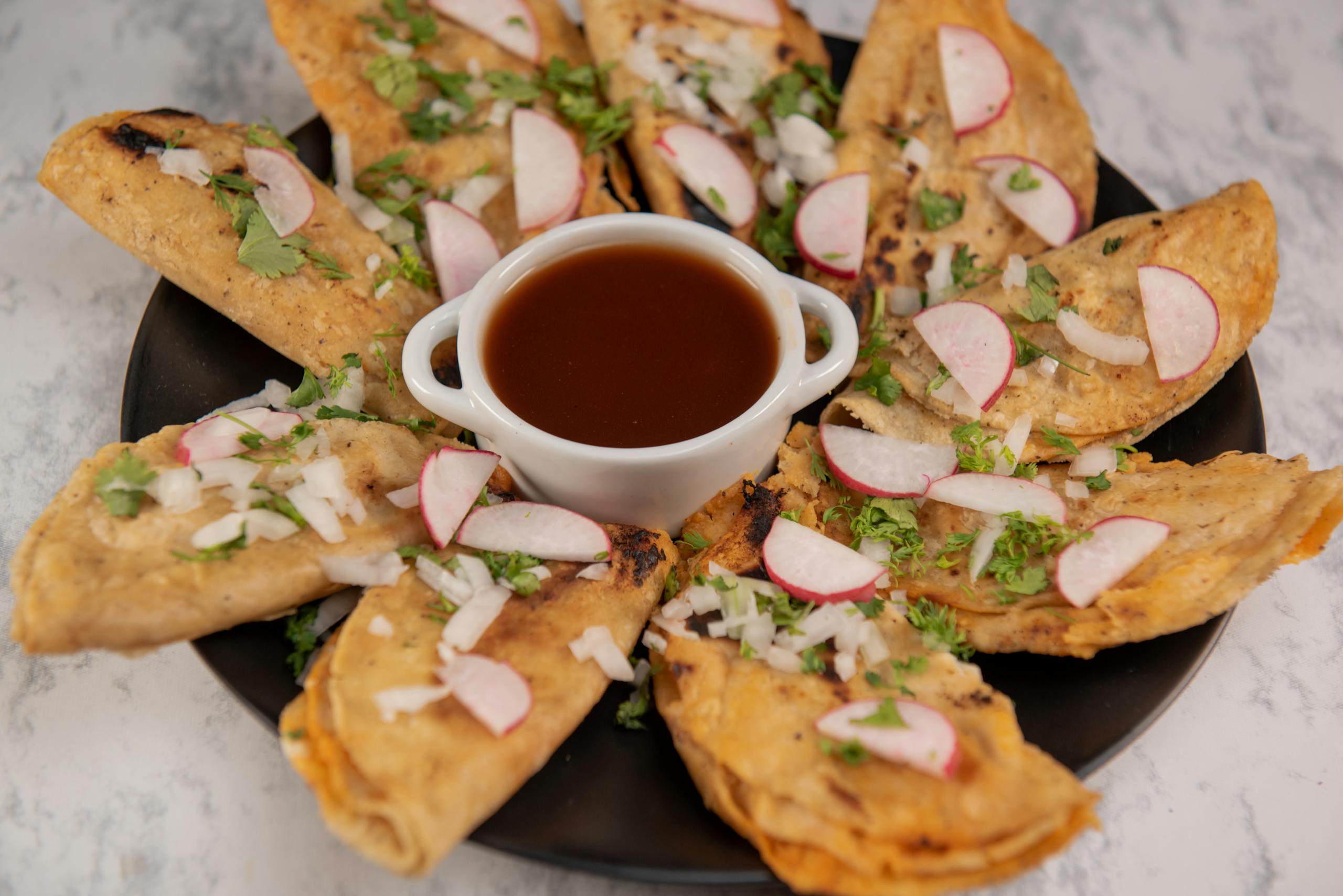 Close-up of Mexican street tacos with salsa, garnished with radish and cilantro on a marble background.
