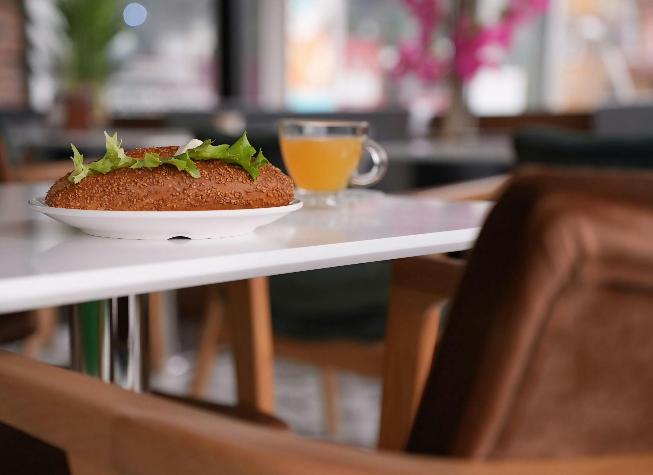A simit with lettuce on a plate and a cup of tea on a cozy café table.