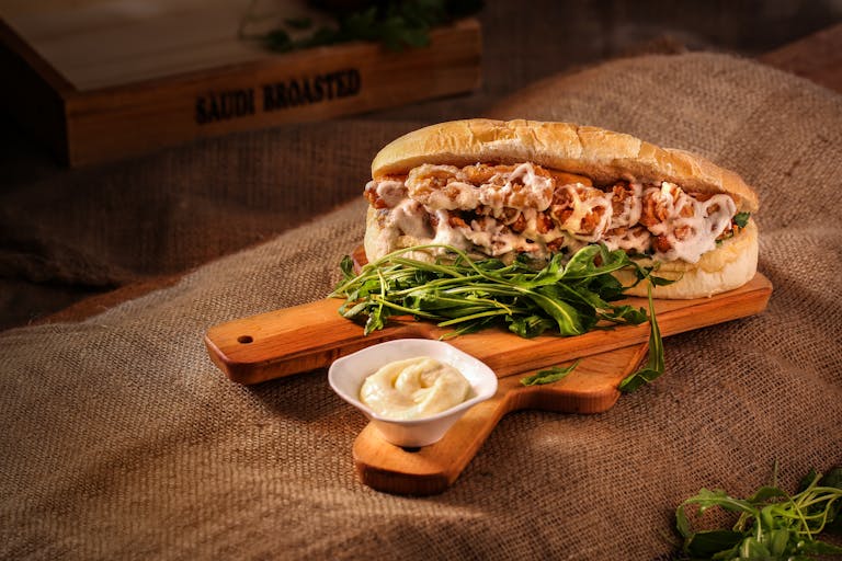 Mouth-watering chicken sandwich with greens on a rustic wooden board.